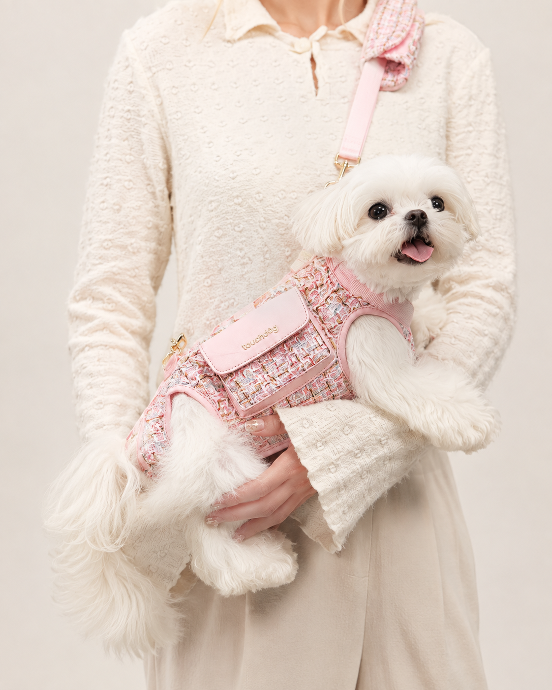 Small white dog wearing pink tweed pet carrier bag with adjustable shoulder strap
